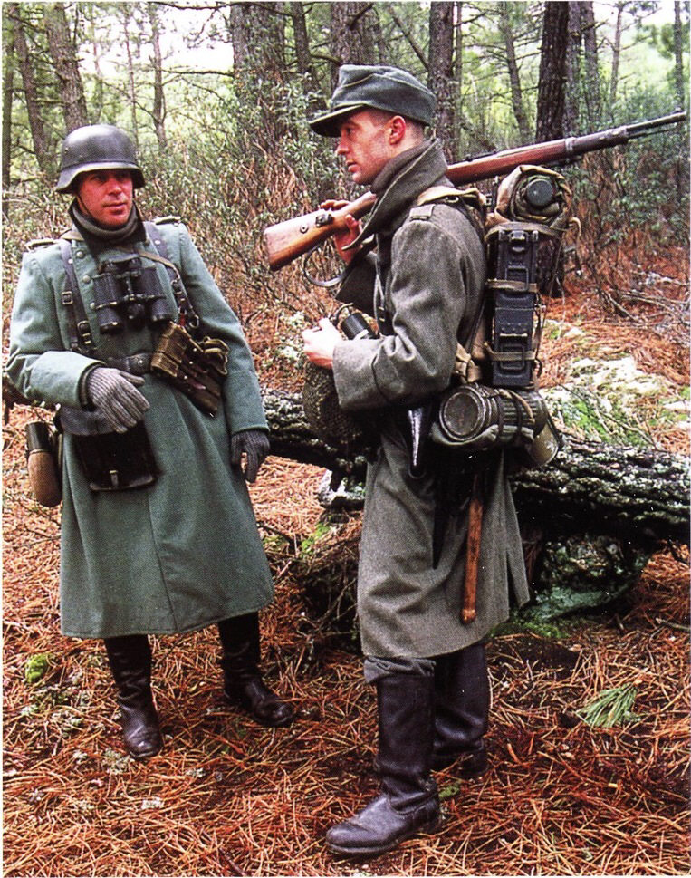 солдат справа вооружен карабином и пистолетом. У него зa спиной две коробки с боеприпасами